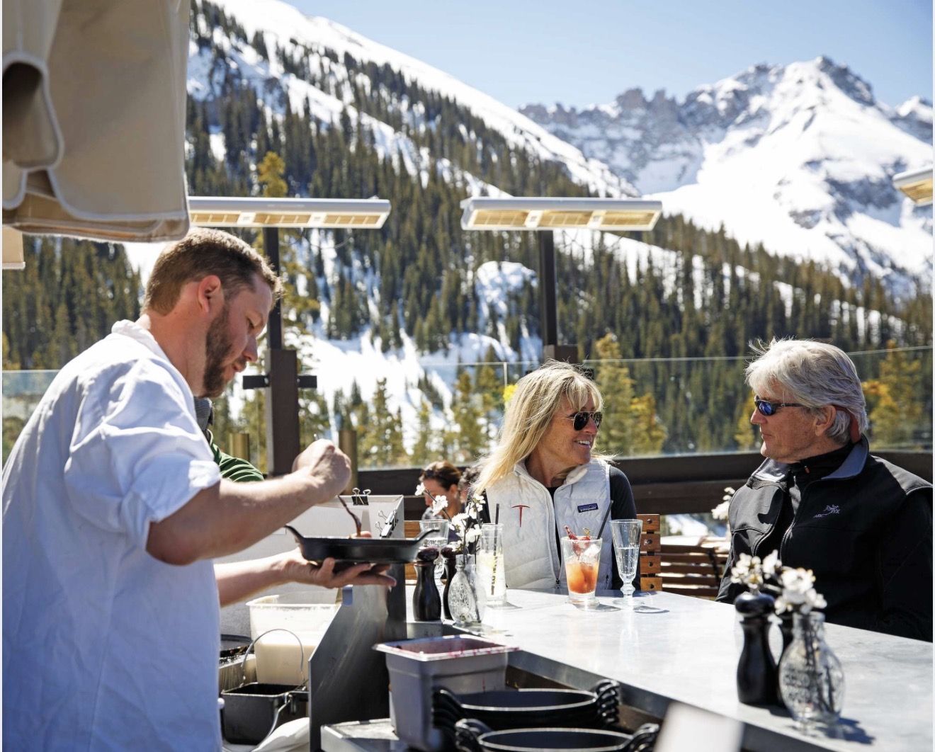 A chef plating a dish at the counter at Bon Vivant with guests seated at the bar
