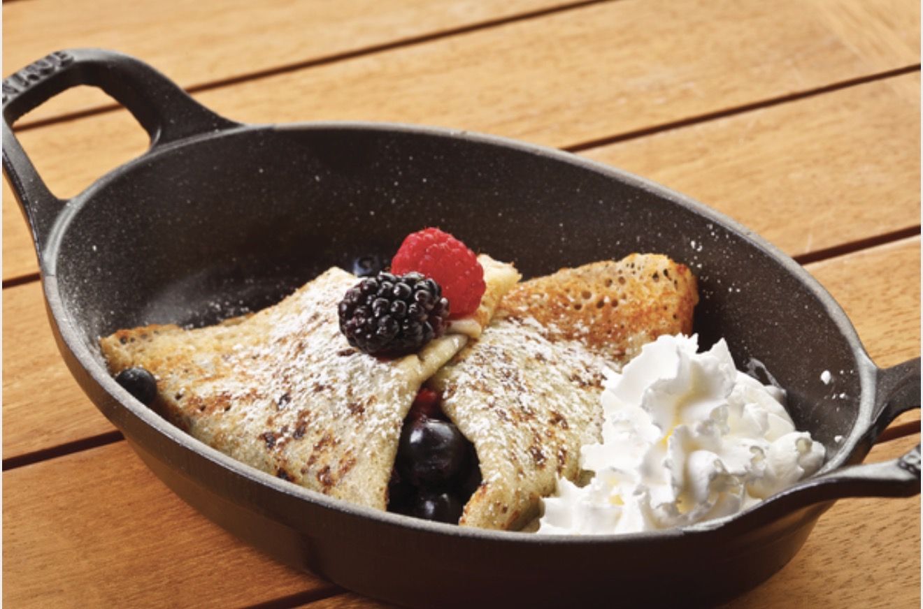 A berry crepe dusted with sugar, served in a cast-iron skillet