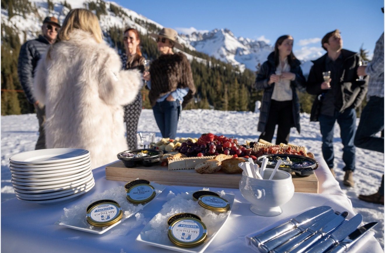 A private gathering on the snow at Bon Vivant, caviar service and a charcuterie spread laid out with guests and the San Juan peaks behind