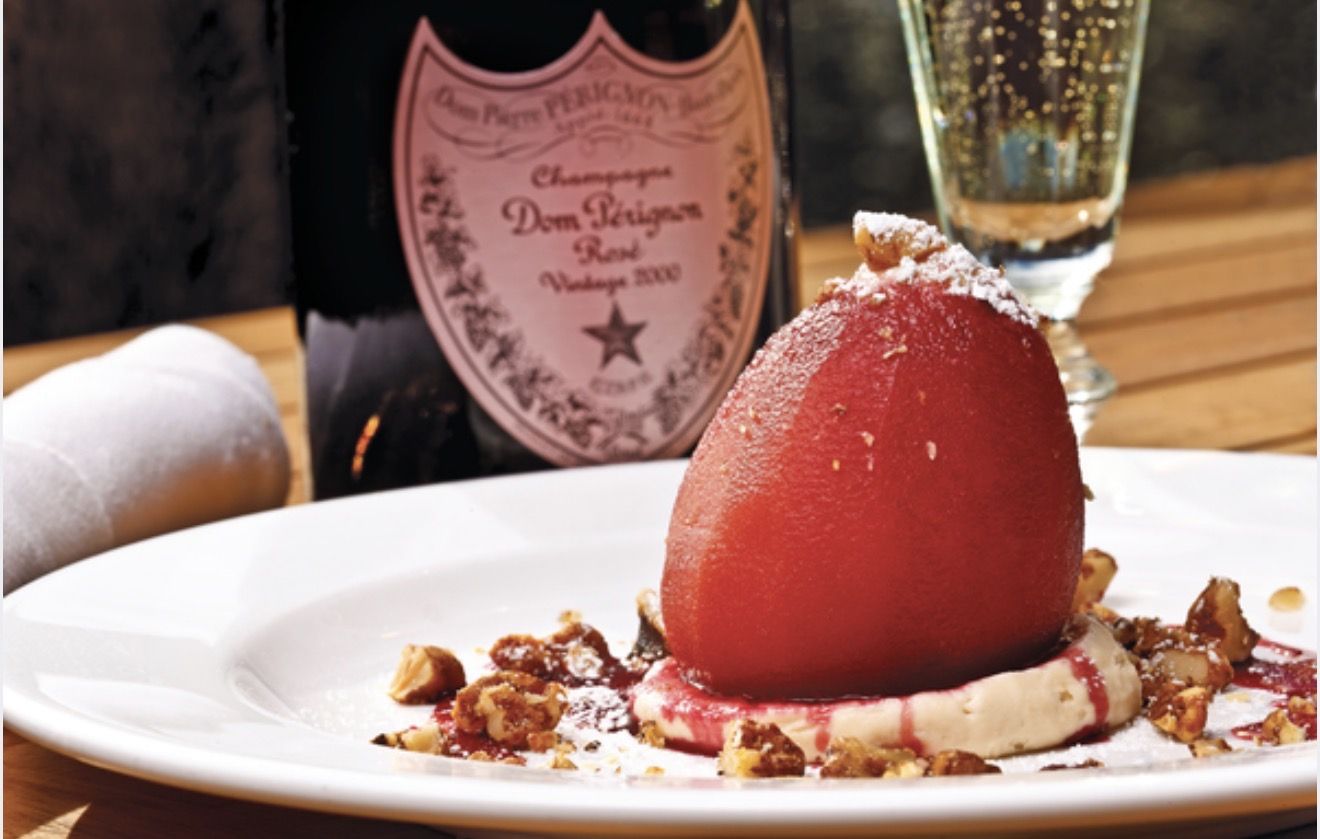 A poached pear dessert beside a bottle of vintage rose champagne at Bon Vivant