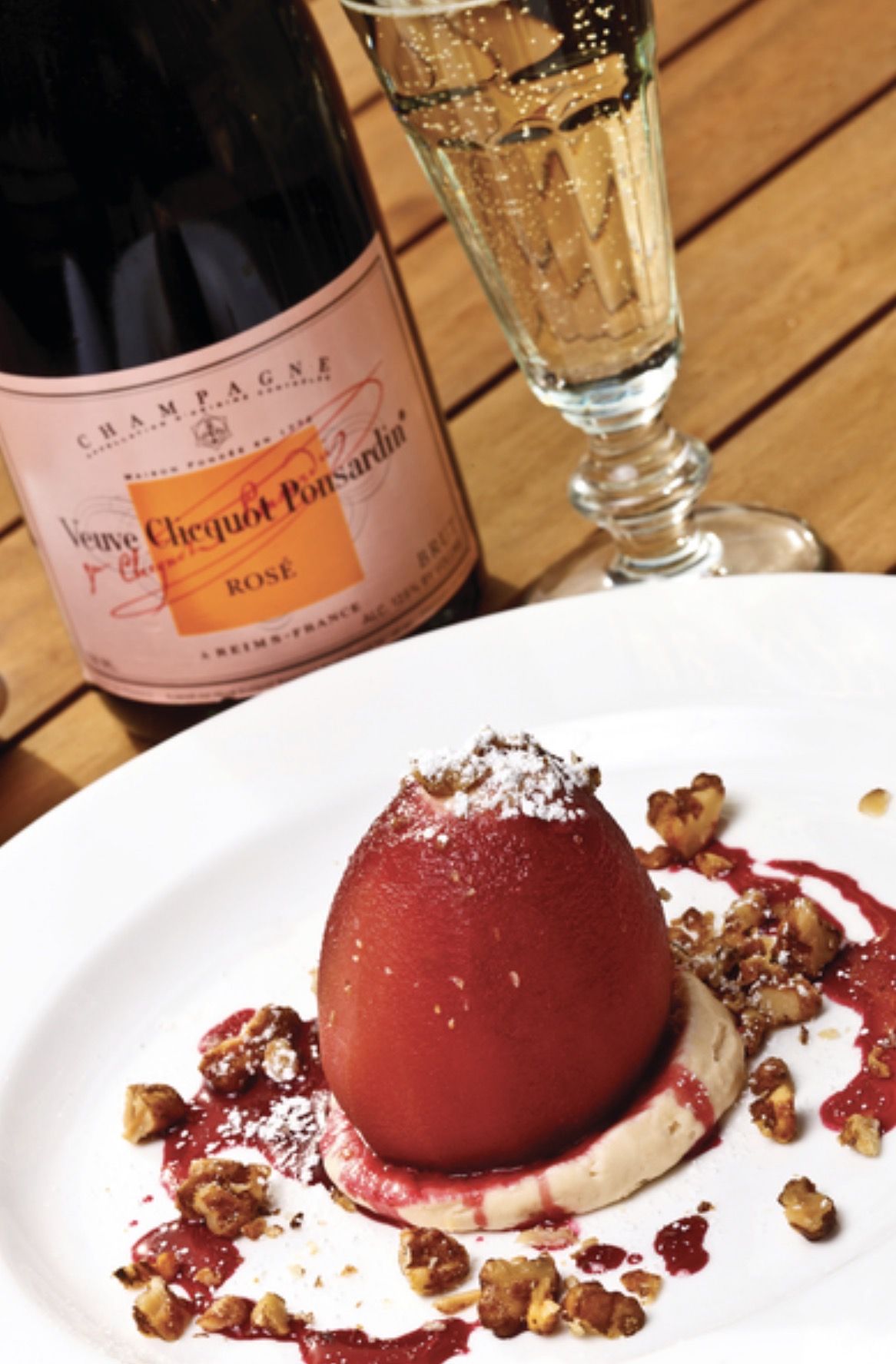 A poached pear dessert beside a bottle of rose champagne on the deck at Bon Vivant